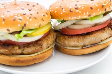 Domatesli, soğanlı, beyaz tabakta salatalıklı büyük bir hamburger manzarası.
