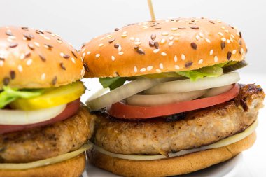 Domatesli, soğanlı, beyaz tabakta salatalıklı büyük bir hamburger manzarası.