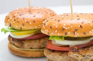 Domatesli, soğanlı, beyaz tabakta salatalıklı büyük bir hamburger manzarası.