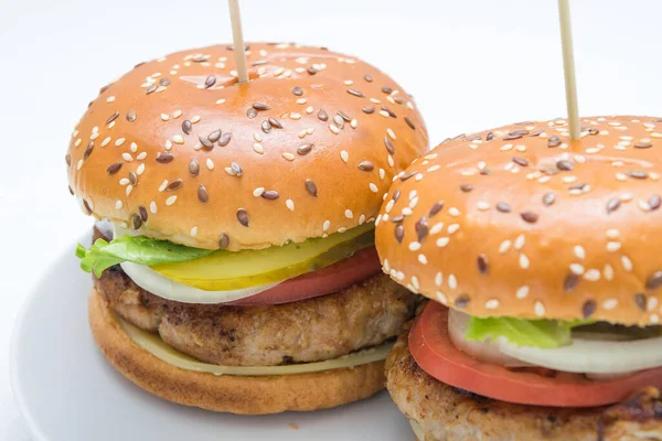 Domatesli, soğanlı, beyaz tabakta salatalıklı büyük bir hamburger manzarası.