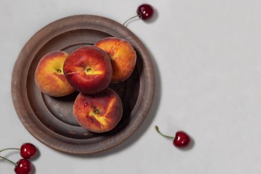 Kil tabakta kırmızı-sarı şeftali ve açık gri arka planda birkaç kiraz. Yukarıdan bak. Sağ tarafta boş alan