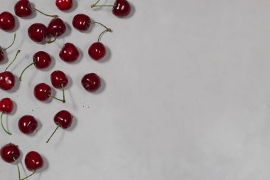 Koyu kırmızı ve koyu kırmızı kirazlar sol tarafta gri arka planda. Sağ tarafta boş yer var. Düz ley, üst görünüm