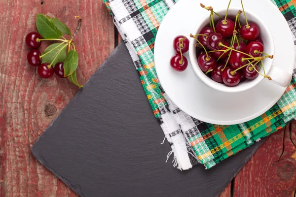 Cerejas no copo branco na mesa de madeira — Fotografia de Stock