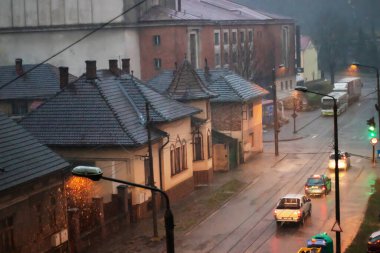 Yağmurlu bir akşamda şehrin en iyi manzarası. Fenerlerin sarı ışığı yağmur damlalarına yansıyor, aynı zamanda sokakta giden arabaların farlarının ışığına da.