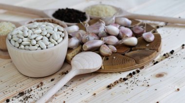 Geleneksel ahşap masa ortasında sarımsak karanfilleri, pişirmek için bir kase fasulye, ve arka planda iki ahşap kaşık biber ve pirinç