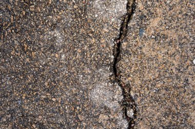 Eski asfaltta geniş bir çatlak var. Çeşitli küçük taşlar ve bir taraftan diğer tarafa bir çatlak görünüyor.