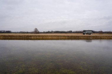 İlkbaharın başlarında, Letonya kırsalında kar yeni eridiğinde ve büyük su birikintisinin arkasında bir orman görülebildiğinde sular altında kalan çayır.