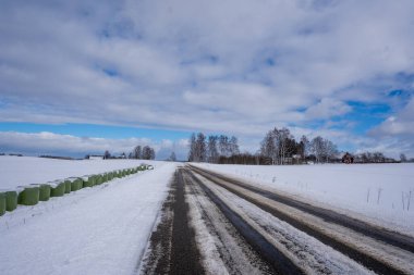 Yol kışın beyaza döndü ve sürmesi zordur çünkü üzerinde iki karanlık yükseliş vardır, ama arka planda arkasında mavi gökyüzü olan bir ev vardır..