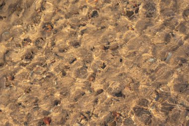 Su kıvrılır ve içinden sarı kum ve küçük taşları görebileceğiniz bir doku oluşturur.