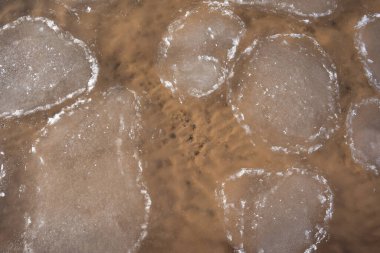 Su kıvrılır ve içinden sarı kum ve küçük taşları görebileceğiniz bir doku oluşturur.