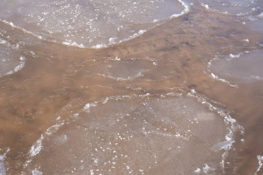 Su kıvrılır ve içinden sarı kum ve küçük taşları görebileceğiniz bir doku oluşturur.