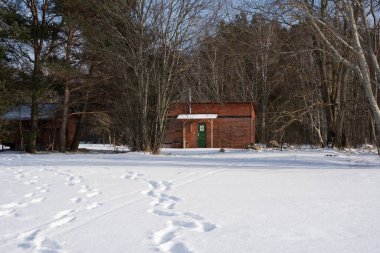 Arkasında karlı bir tarla var. Karlı bir çatısı ve ağaçları olan bir ev.