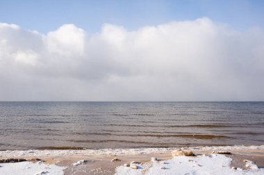 Mavi gökyüzü ile Letonya Baltık Denizi ve beyaz karla kaplı kumsaldaki beyaz bulutlar