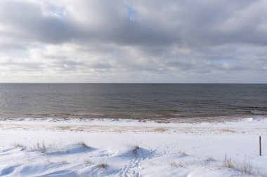 Mavi gökyüzü ile Letonya Baltık Denizi ve beyaz karla kaplı kumsaldaki beyaz bulutlar