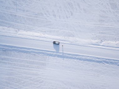 Top down view where you can see the car on a white snowy field where there is a road and a person is standing on it