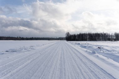 A warm and sunny snowy winter day with a country road driven by cars and there are rises left