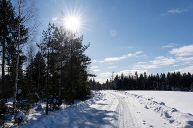 a beautiful sunny winter day in the Latvian countryside with blue skies and white clouds where there is a road in the middle of the field that is covered with snow and on which the tracks of car tires remain in the snow