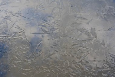 thin ice is frozen on the water, which forms an interesting texture and reflections, through the thin ice you can see the bed of the water body, which is lighter and darker
