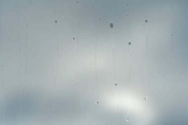 close up of the car glass where water droplets and various dirt have run off but in the background there is a blurred sky with clouds behind which the sun is