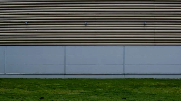 a large hangar wall where the cladding runs horizontally and the green grass is in the foreground