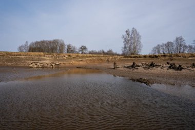 Balık çiftliği göleti su seviyesine indirilir ve bazı ağaç gövdeleri ve taşlarla yatağını görünür hale getirir.