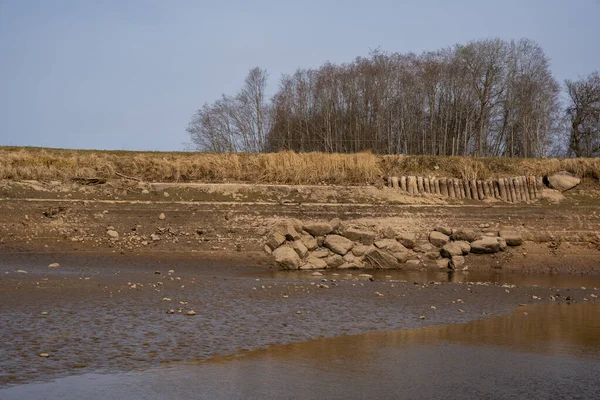 The pond for fish farming is lowered to the water level and visible its bed with some tree trunks and stones