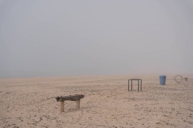 The beach of the Baltic Sea in Ventspils, where there is a thick fog, you can only see benches and rubbish bins placed in the sea sand