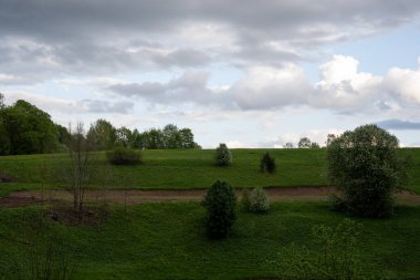 Ağaçlarla ve üzerinde güzel bir gökyüzü olan yeşil otlarla dolu dağlık bir arazi.