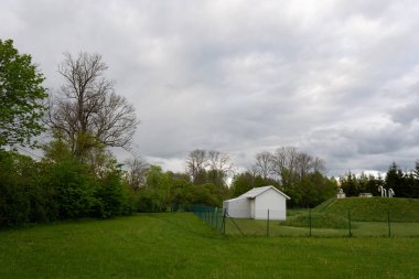 Yeşil alanda çitleri olan küçük beyaz bir bina var.
