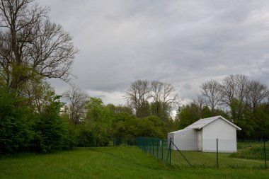 Yeşil alanda çitleri olan küçük beyaz bir bina var.