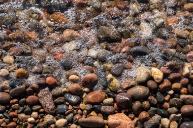 Baltık Denizi kıyılarında farklı renklerde taşlar vardır. Resmin bir kısmının köpüren bir dalgayla kaplı olduğu güzel bir desen oluştururlar.