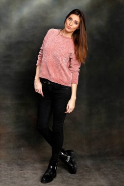 Güzel, pozitif esmer kız stüdyoda tuvalin arka planında poz veriyor. Rahatlama, zarafet, moda konsepti.