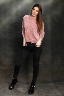 Güzel, pozitif esmer kız stüdyoda tuvalin arka planında poz veriyor. Rahatlama, zarafet, moda konsepti.