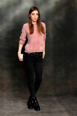 Güzel, pozitif esmer kız stüdyoda tuvalin arka planında poz veriyor. Rahatlama, zarafet, moda konsepti.