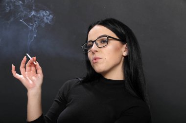 Siyah saçlı, gözlüklü, stüdyoda poz veren ve arka planda puro içen çekici Avrupalı bir kız. Tarz, trendler, sigara konsepti
