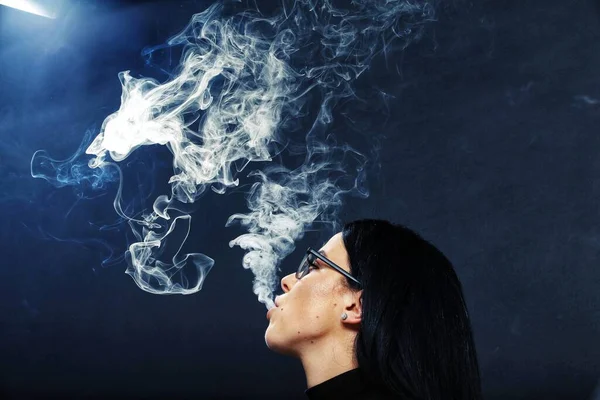迷人的欧洲姑娘 黑头发 戴着眼镜 在工作室里摆姿势 在孤立的背景下抽一支雪茄 吸烟概念 — 图库照片