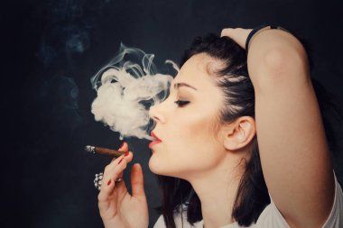 Güzel Avrupalı otoriter esmer kız izole bir arka planda stüdyoda patron gibi sigara içiyor. Modellik, tarz, moda konsepti. Kara etki