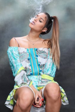 Güzel esmer kadın model stüdyoda poz veriyor ve izole edilmiş arka planda elektrikli puro içiyor. Tarz, sigara, moda konsepti.
