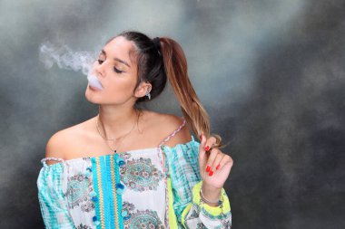 Güzel esmer kadın model stüdyoda poz veriyor ve izole edilmiş arka planda elektrikli puro içiyor. Tarz, sigara, moda konsepti.