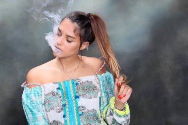 Güzel esmer kadın model stüdyoda poz veriyor ve izole edilmiş arka planda elektrikli puro içiyor. Tarz, sigara, moda konsepti.