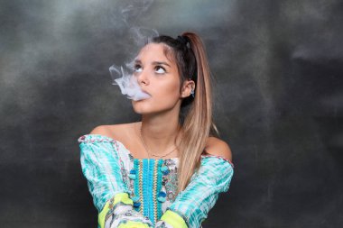 Güzel esmer kadın model stüdyoda poz veriyor ve izole edilmiş arka planda elektrikli puro içiyor. Tarz, sigara, moda konsepti.