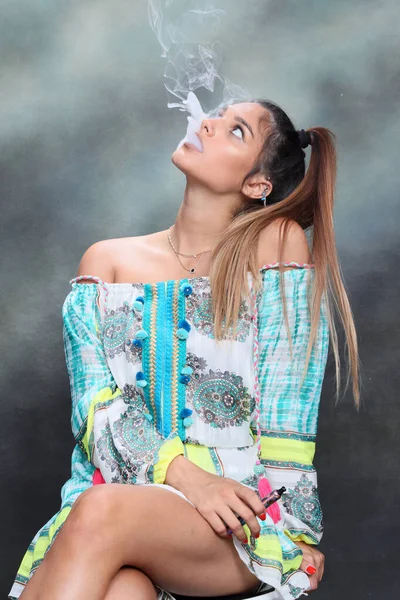 Güzel esmer kadın model stüdyoda poz veriyor ve izole edilmiş arka planda elektrikli puro içiyor. Tarz, sigara, moda konsepti.