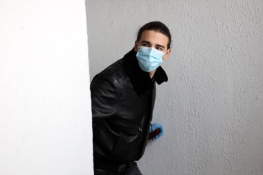 Corona virüsü yüzünden koruyucu maske ve eldiven takan uzun saçlı çekici bir genç. Güvenlik, koruma, Covid-19 konsepti.