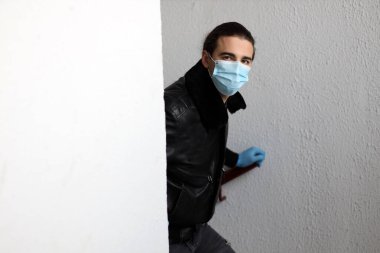 Corona virüsü yüzünden koruyucu maske ve eldiven takan uzun saçlı çekici bir genç. Güvenlik, koruma, Covid-19 konsepti.