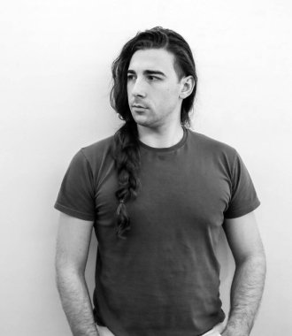 Saçları örgülü çekici genç adam balkonda poz veriyor. Tarz, trendler, moda konsepti.