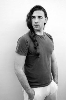 Saçları örgülü çekici genç adam balkonda poz veriyor. Tarz, trendler, moda konsepti.