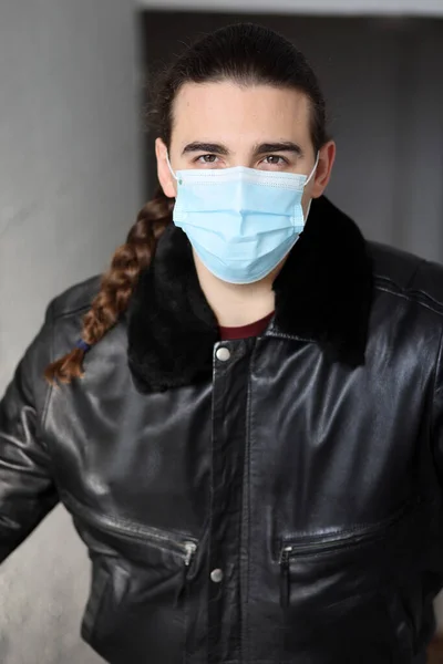 Young attractive guy with long hair wearing a protective medical mask and gloves due to Corona virus. Safety, protection, Covid-19 concept.