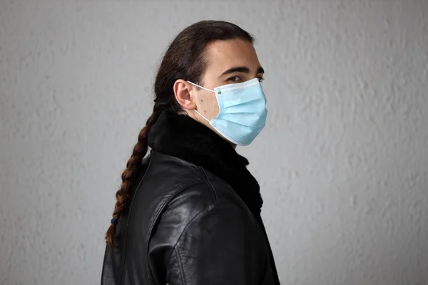 Young attractive guy with long hair wearing a protective medical mask and gloves due to Corona virus. Safety, protection, Covid-19 concept.