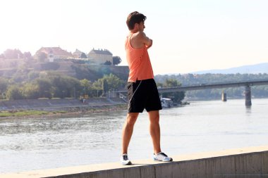 Young male athlete exercising by the Danube river at quay in Novi Sad, Serbia. Healthy lifestyle, outdoor running, sports concept. clipart