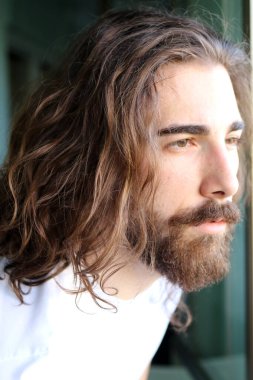 Uzun saçlı ve sakallı şık, beyaz bir adam balkonda poz veriyor. Tarz, trendler, moda konsepti.